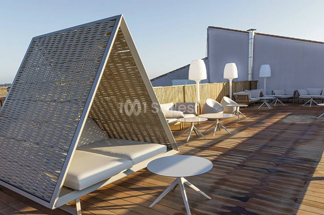 Terrasse en bois avec mobilier moderne, incluant un lit de repos triangulaire et des lampes blanches.