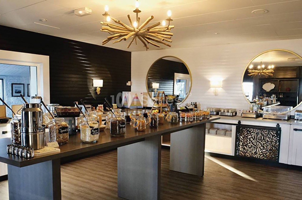 Buffet de petit-déjeuner avec céréales, boissons et viennoiseries, présenté dans une salle lumineuse et moderne.