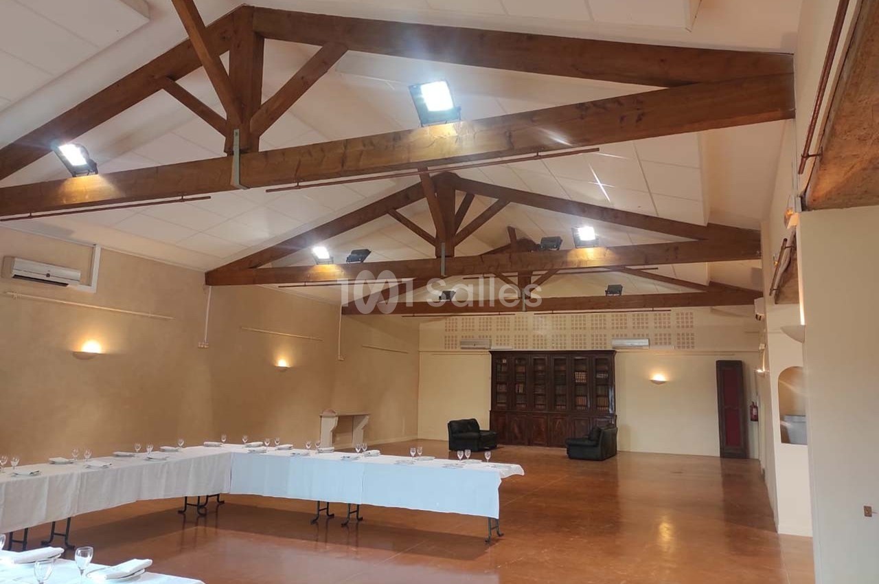 Salle spacieuse avec poutres apparentes, tables dressées pour un événement et éclairage au plafond.