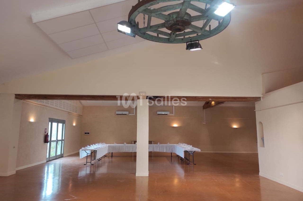 Salle spacieuse avec un sol en béton ciré, une grande table dressée au fond et un lustre en bois suspendu au plafond.