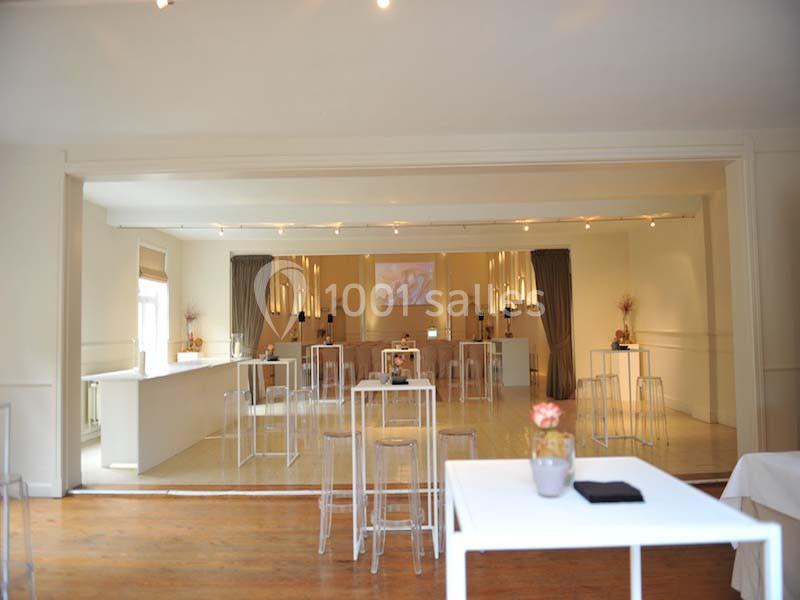 Salle lumineuse aménagée avec des tables hautes, des tabourets transparents et une décoration minimaliste.