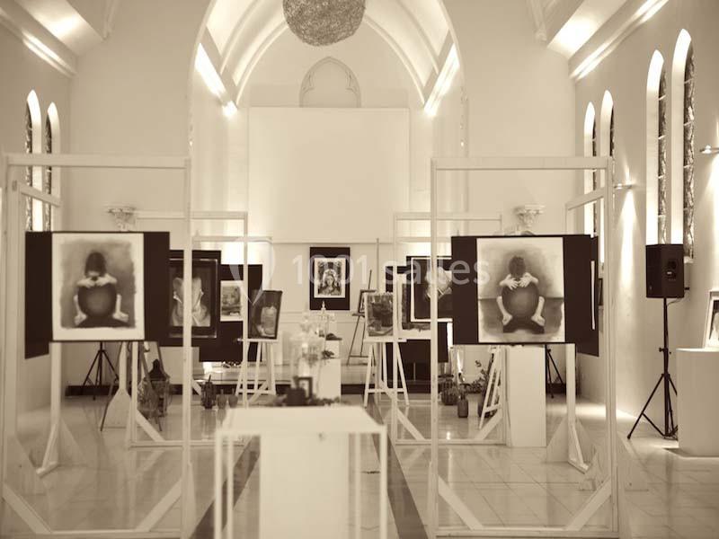 Exposition artistique dans une salle lumineuse avec des photographies en noir et blanc disposées sur des chevalets.