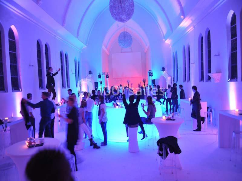 Personnes dans une salle éclairée de lumières violettes, dansant et socialisant autour de tables hautes.