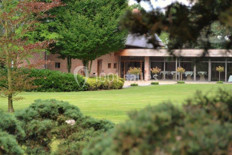 Vue d'un bâtiment en briques entouré d'arbres et d'un jardin avec une pelouse bien entretenue.