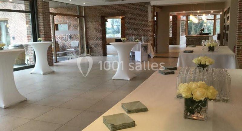 Salle lumineuse avec tables hautes couvertes de nappes blanches, décorée de bouquets de roses blanches.