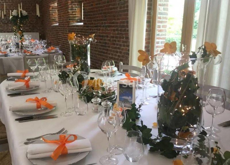 Table décorée pour un événement avec nappes blanches, fleurs orange, rubans assortis et verrerie élégante.
