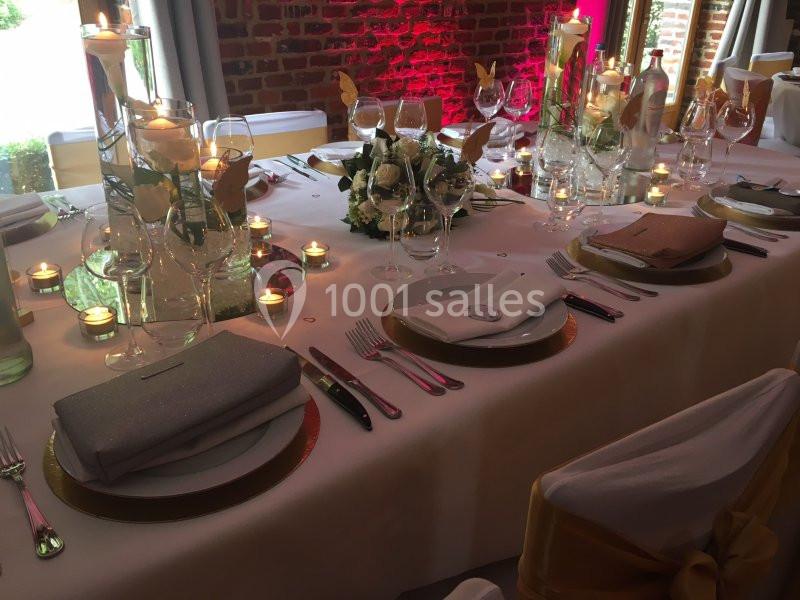 Table élégamment dressée avec nappes blanches, vaisselle raffinée, bougies allumées et décoration florale.