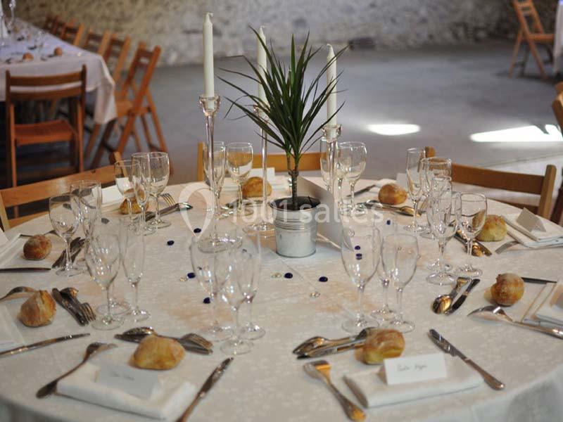 Table dressée pour un repas, avec nappes blanches, couverts, verres, bougies et une plante en centre de table.