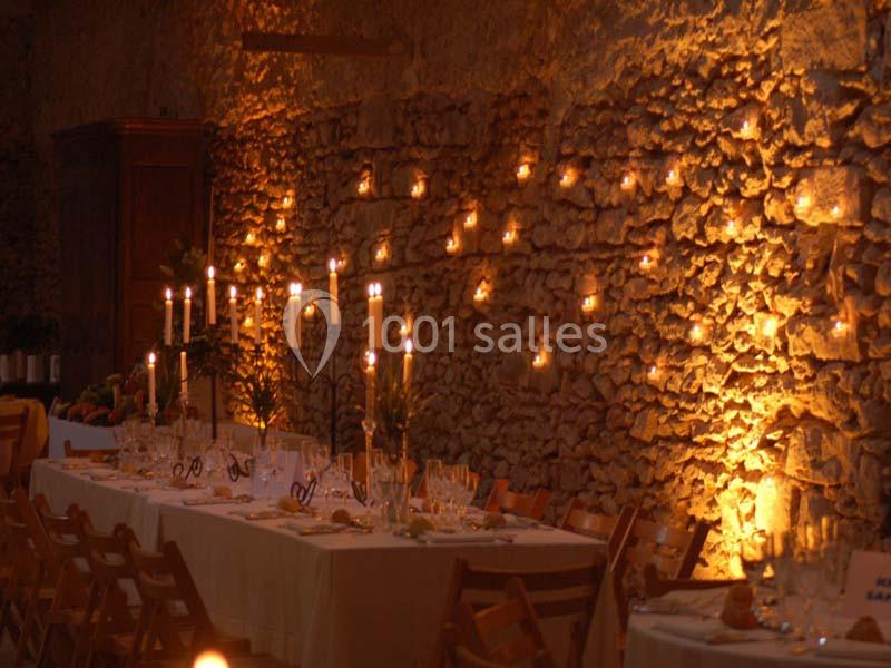 Salle en pierre éclairée par des bougies, avec une longue table dressée pour un repas convivial.