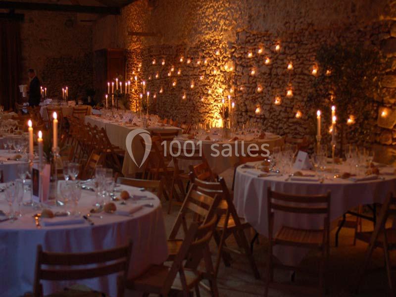 Salle de réception décorée avec des tables rondes, nappes blanches, chandeliers et guirlandes lumineuses sur un mur en…