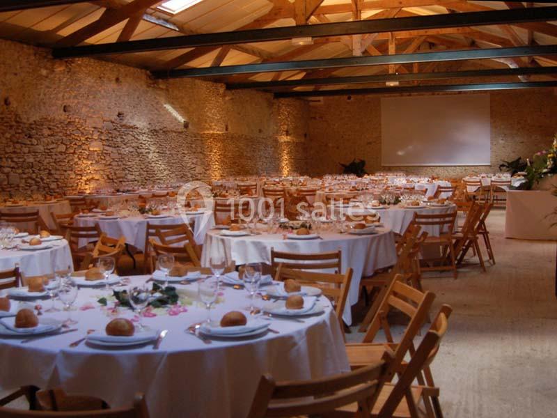 Salle de réception en pierre avec des tables rondes dressées pour un événement, éclairage chaleureux.