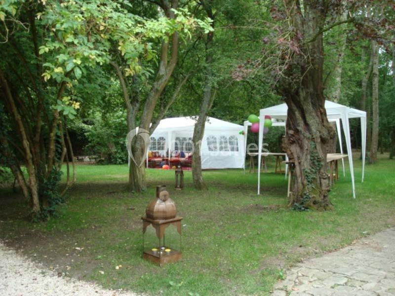 Deux tentes blanches installées dans un jardin verdoyant avec des arbres et une décoration simple.
