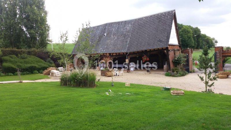 Grange ouverte avec toit en ardoise, entourée de verdure et aménagée pour un événement avec des tables et décorations.