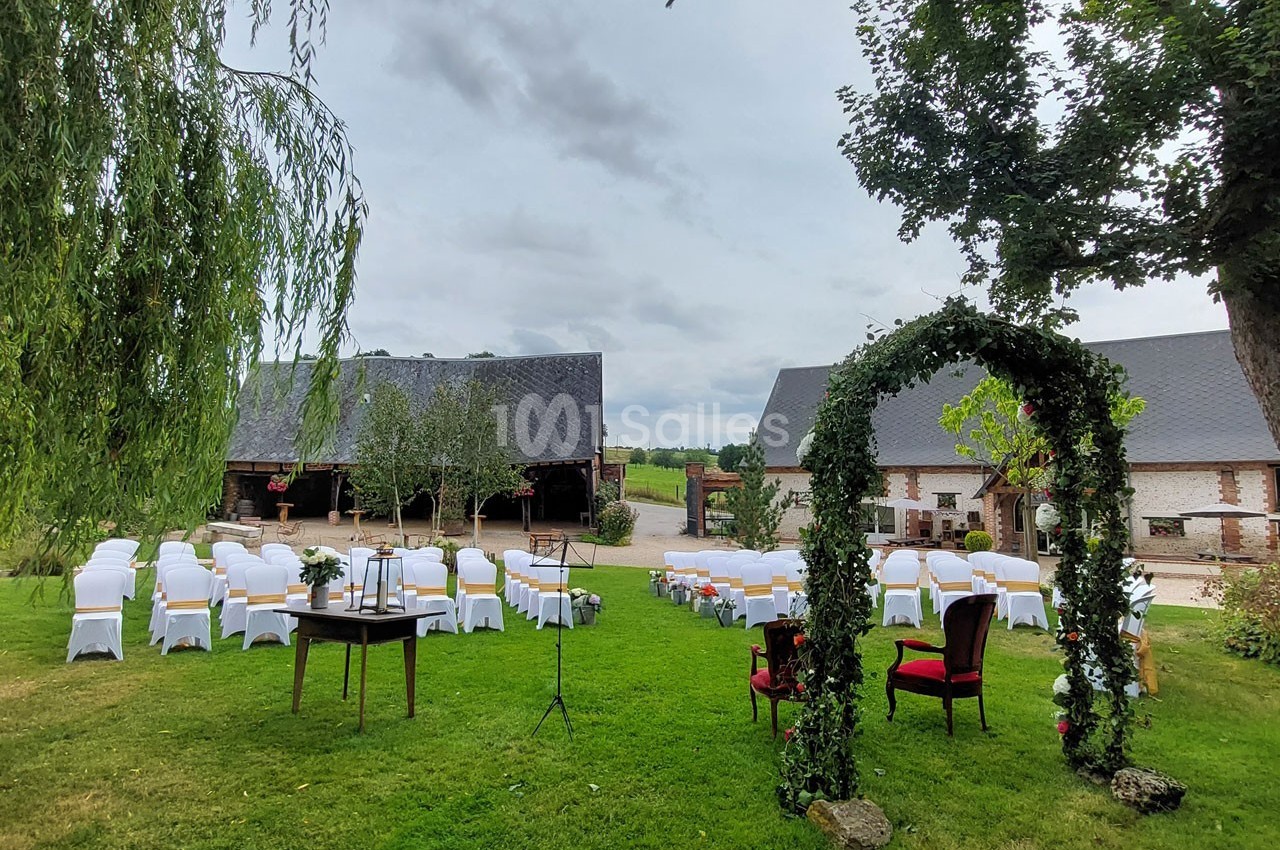 Chaises blanches disposées en extérieur devant une arche végétale, avec des bâtiments en briques et un ciel nuageux en…