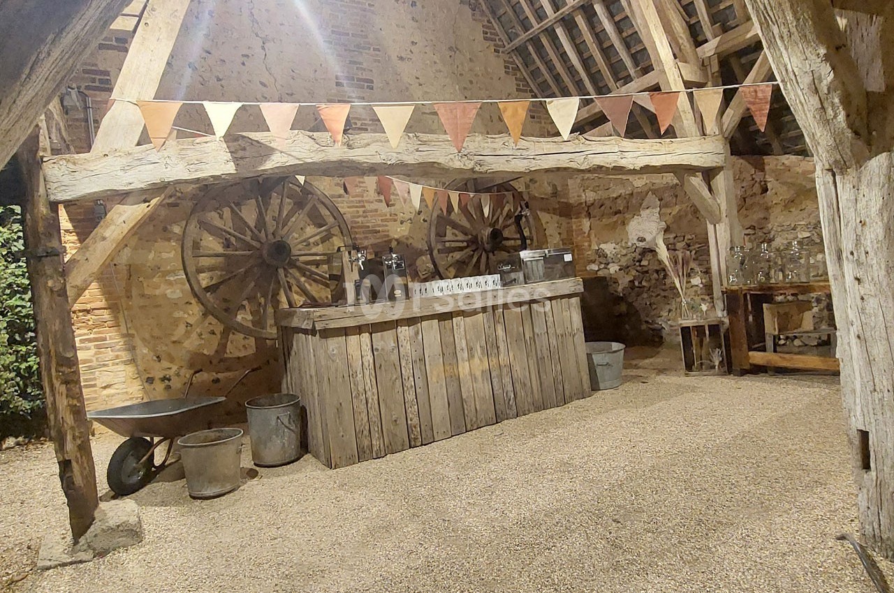 Intérieur d'une grange rustique avec un comptoir en bois, des guirlandes de fanions et des roues en arrière-plan.
