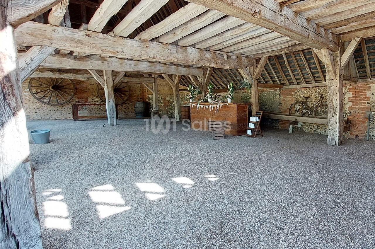 Grange en pierre et bois avec charpente apparente, décorée de fleurs et d'objets rustiques.