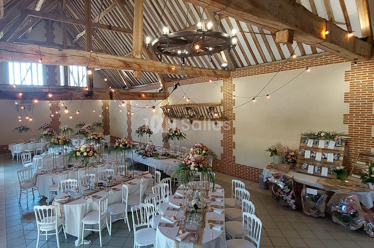 Salle de réception décorée pour un mariage, avec tables dressées, fleurs colorées et guirlandes lumineuses suspendues.