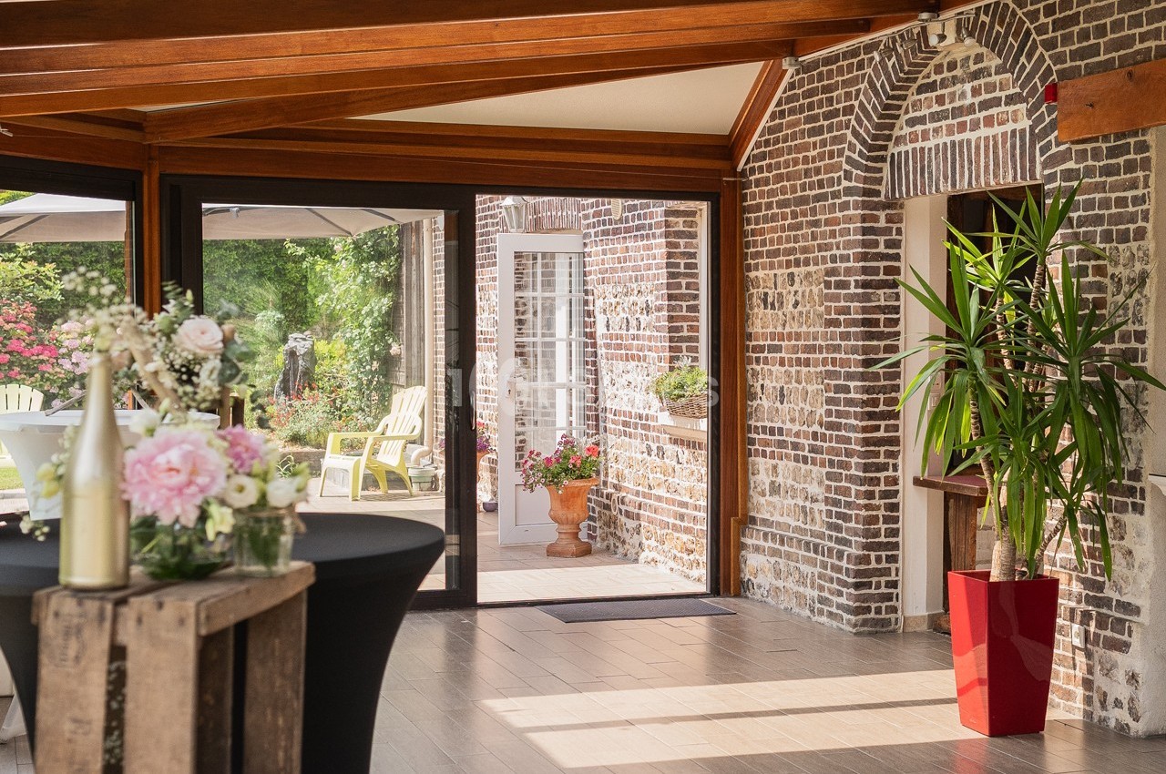 Salle lumineuse avec murs en briques, grandes baies vitrées, plantes décoratives et vue sur un jardin fleuri.