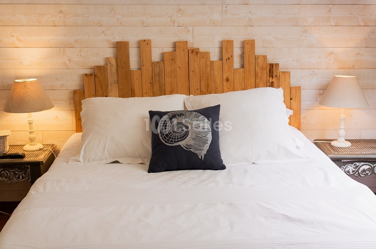 Lit double avec tête de lit en bois, coussin décoratif et deux lampes de chevet sur des tables assorties.