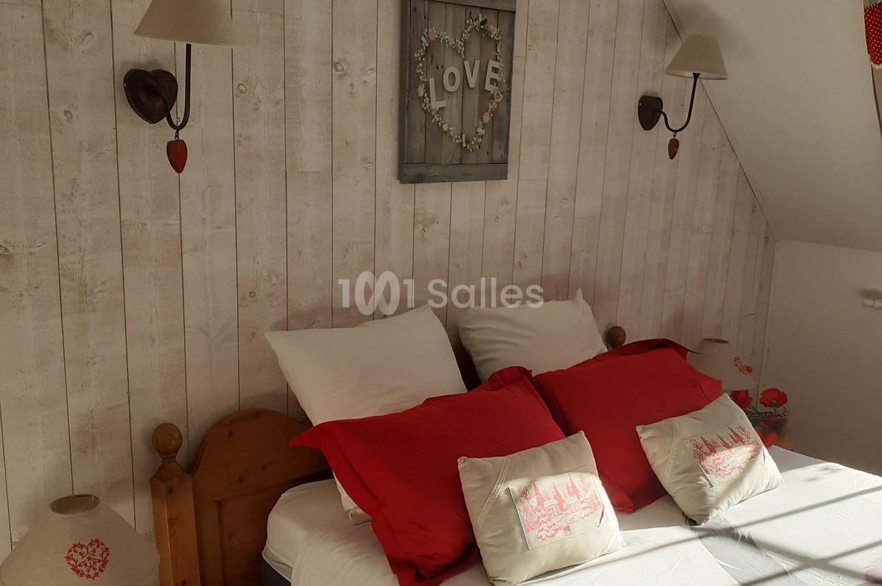 Lit double avec coussins rouges et décorations murales en bois, dans une chambre lumineuse au style rustique.
