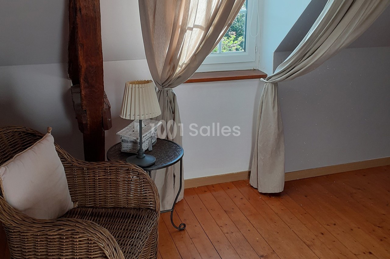 Fauteuil en osier avec coussin, table d'appoint et lampe près d'une fenêtre encadrée de rideaux clairs dans une pièce…