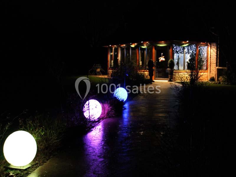 Allée illuminée par des sphères lumineuses colorées menant à une maison éclairée dans la nuit.