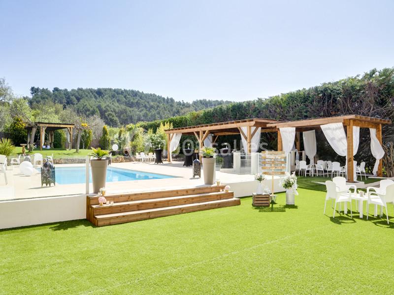 Espace extérieur avec piscine, pelouse, pergolas en bois et chaises blanches, entouré de verdure.