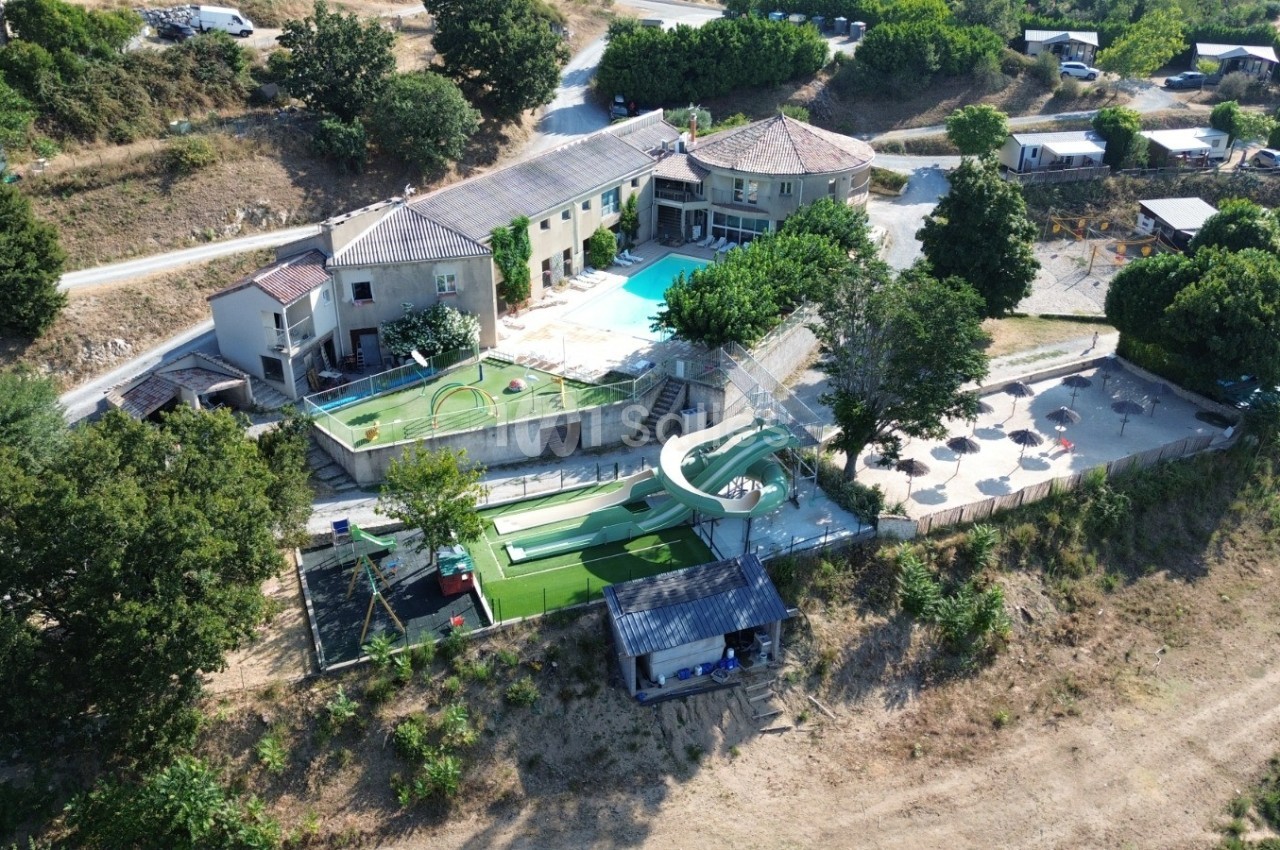 Vue aérienne d'un complexe avec piscine, toboggan aquatique, mini-golf et espaces ombragés entourés de végétation.