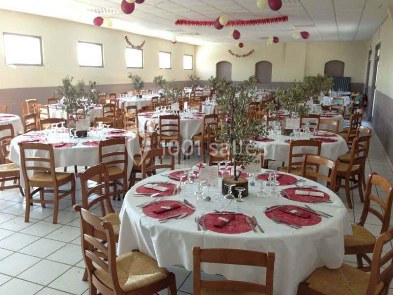 Salle décorée pour un événement avec des tables rondes dressées, nappes blanches, serviettes rouges et centres de table…