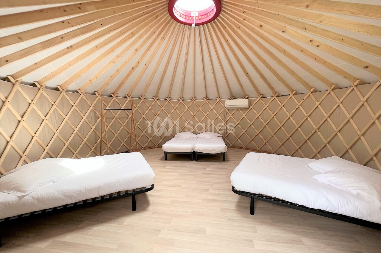 Intérieur d'une yourte avec trois lits simples, sol en bois clair et structure en bois visible.