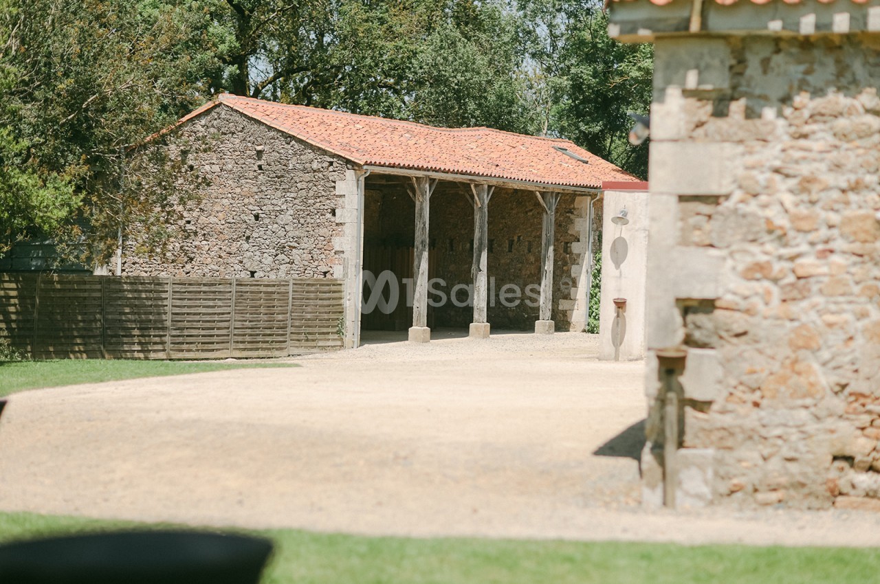 Bâtiment en pierre avec toit en tuiles rouges, entouré d'arbres et d'une cour en gravier.