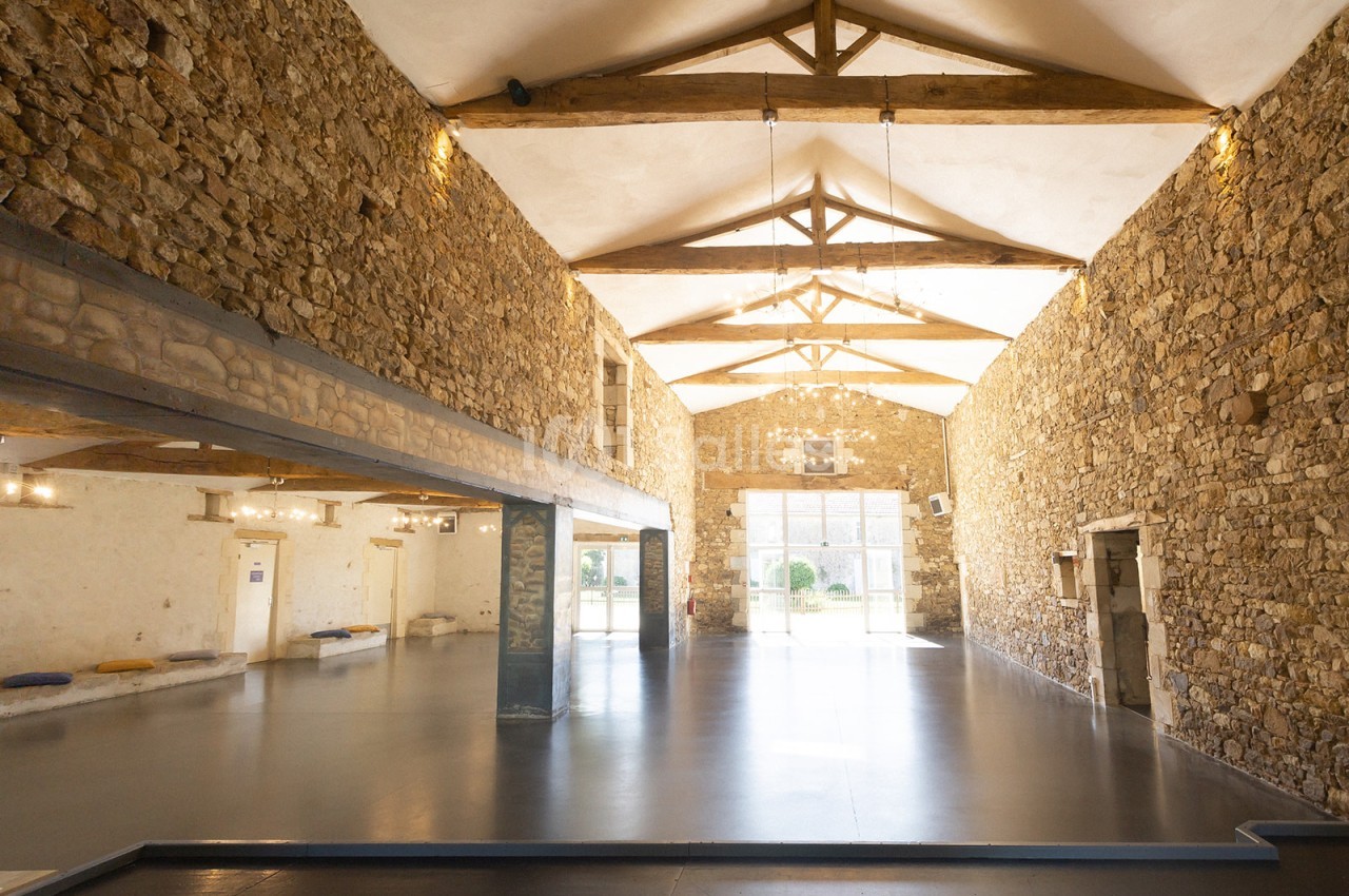 Intérieur d'une grande salle avec murs en pierre apparente, poutres en bois au plafond et sol lisse.