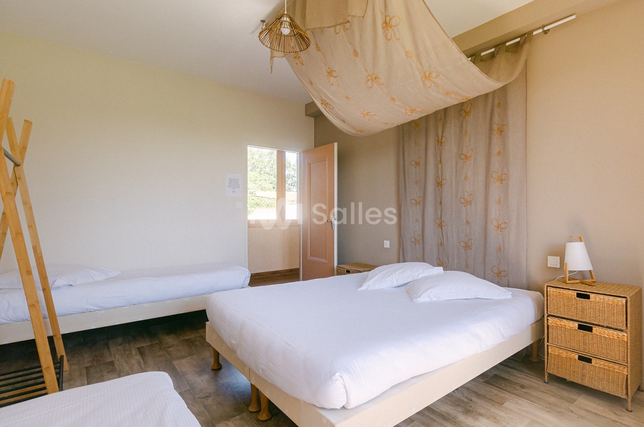 Chambre lumineuse avec trois lits simples, sol en parquet, mobilier en bois clair et rideaux beige décoratifs.