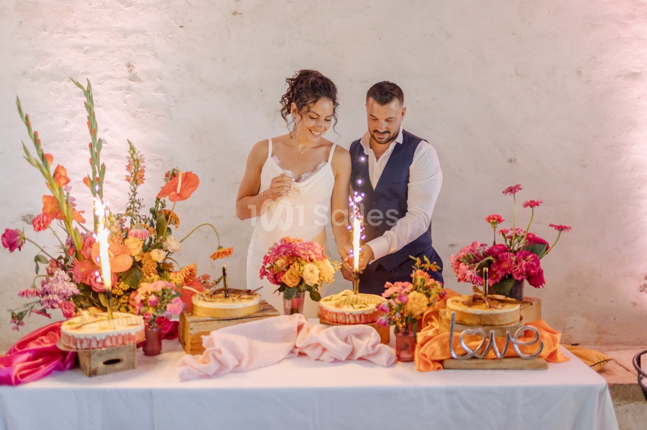 Un couple coupe un gâteau entouré de fleurs colorées sur une table décorée lors d'une célébration.