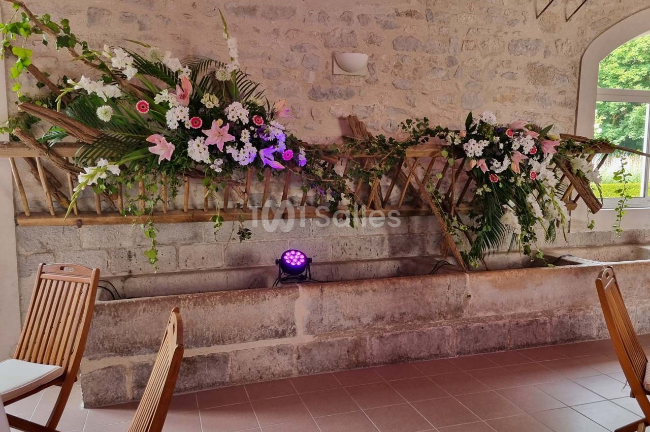 Décoration florale colorée sur une structure en bois contre un mur en pierre, éclairée par une lumière violette.