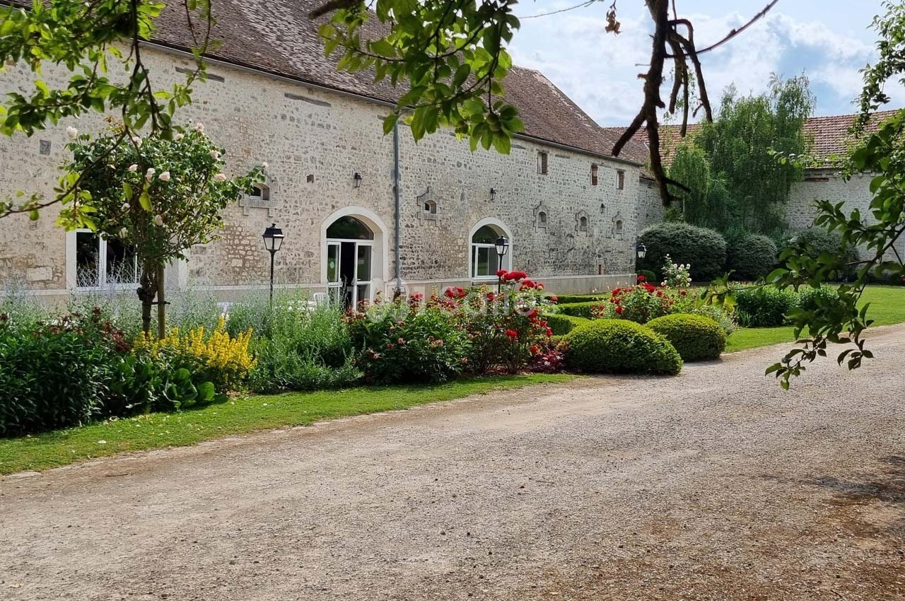 Façade en pierre d'un bâtiment ancien entouré d'un jardin fleuri avec allée gravillonnée au premier plan.