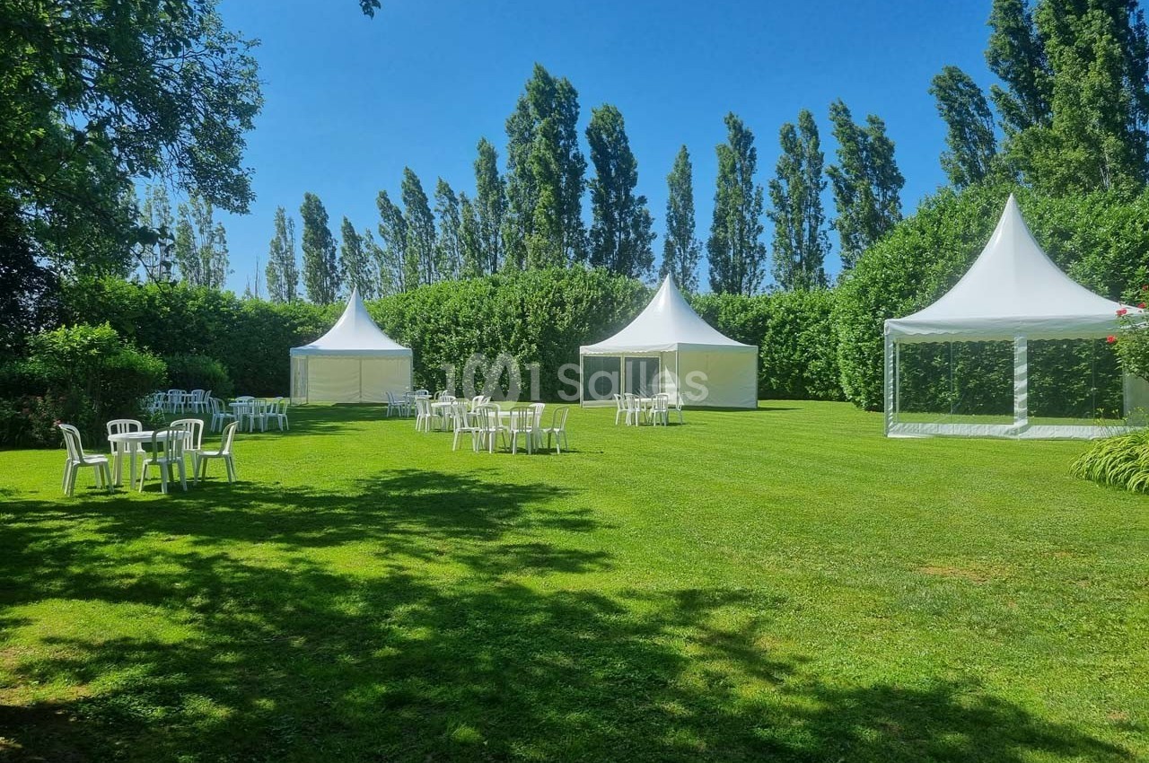 Pelouse verdoyante avec des tentes blanches et des chaises disposées pour un événement en plein air.
