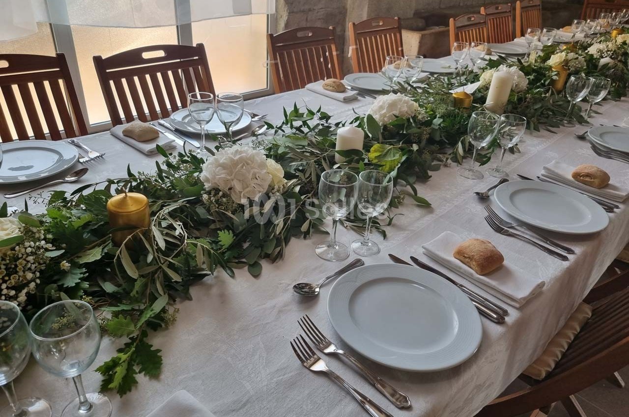 Table dressée avec une nappe blanche, vaisselle, couverts, bougies et décoration florale verte et blanche.