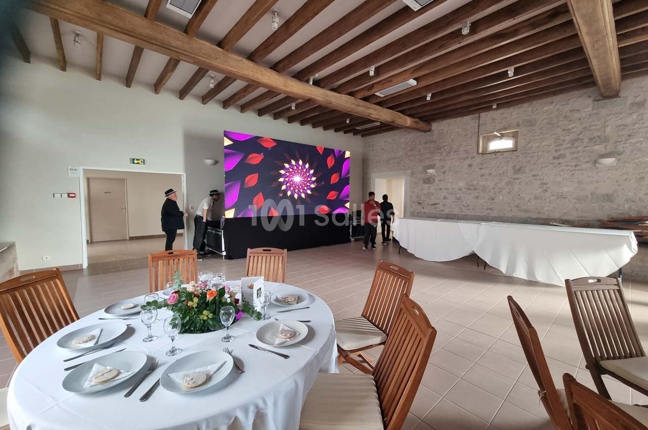 Salle de réception avec tables dressées, écran géant affichant des motifs colorés et murs en pierre apparente.