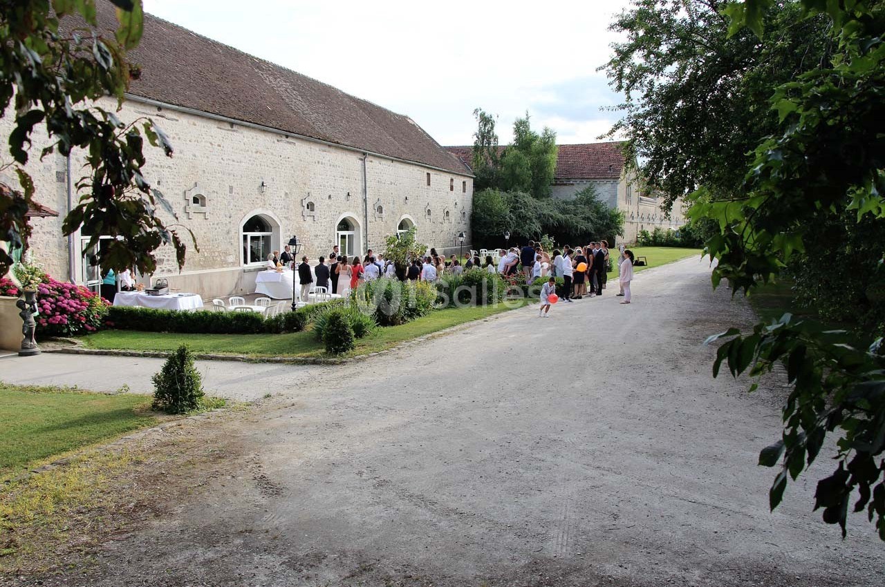 Groupe de personnes rassemblées dans une cour devant un bâtiment en pierre, entouré de verdure.