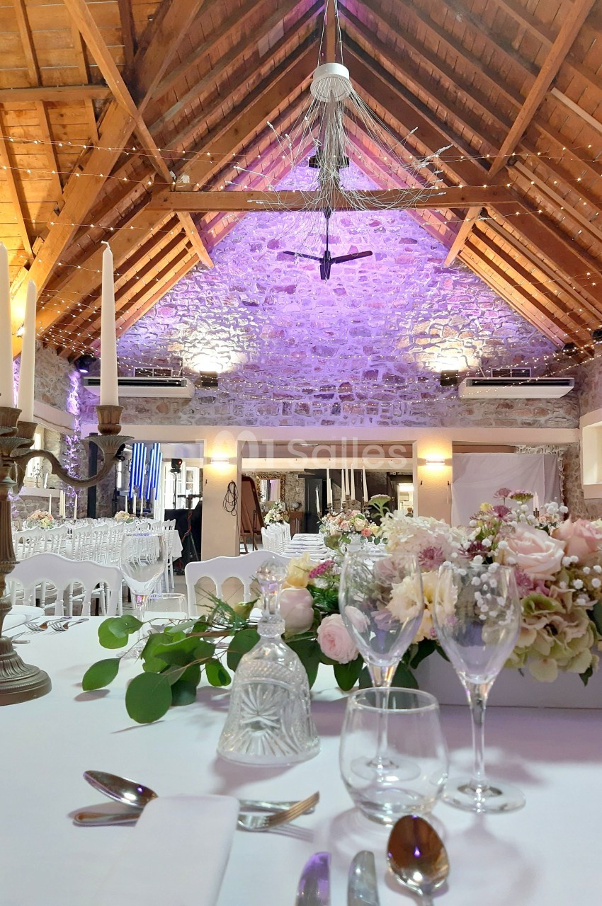 Salle de réception avec poutres apparentes, décor floral sur table dressée et éclairage tamisé.
