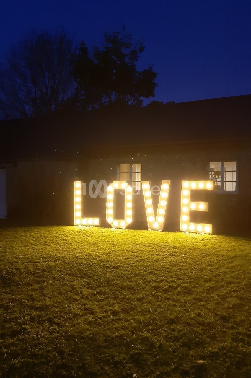 Lettres lumineuses formant le mot ’LOVE’ posées sur une pelouse devant un bâtiment sombre au crépuscule.