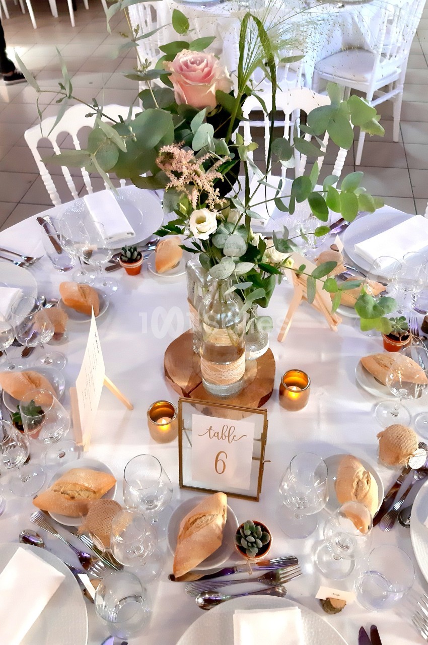 Table de réception décorée avec un centre de table floral, bougies, vaisselle élégante et petits pains disposés.