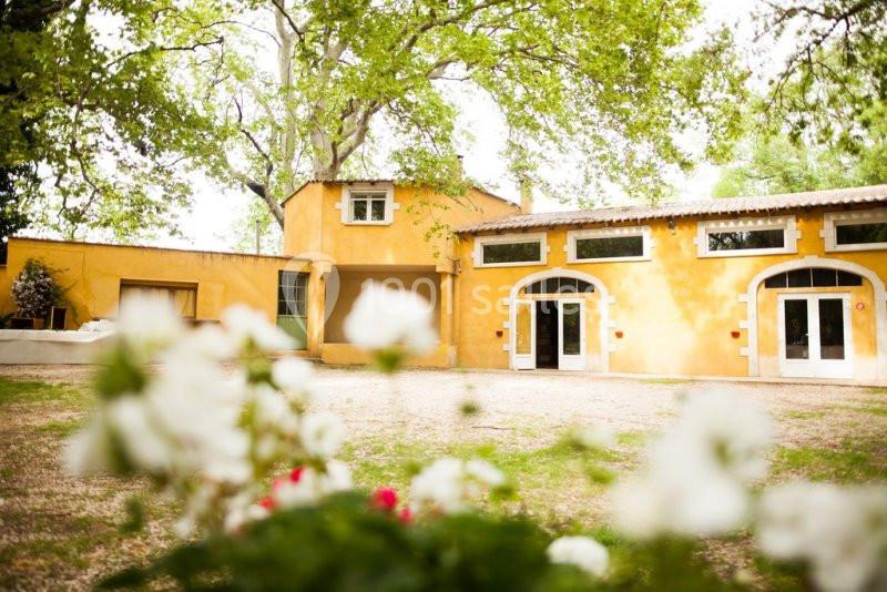 Bâtiment jaune à un étage entouré d'arbres, avec des fleurs floues au premier plan.