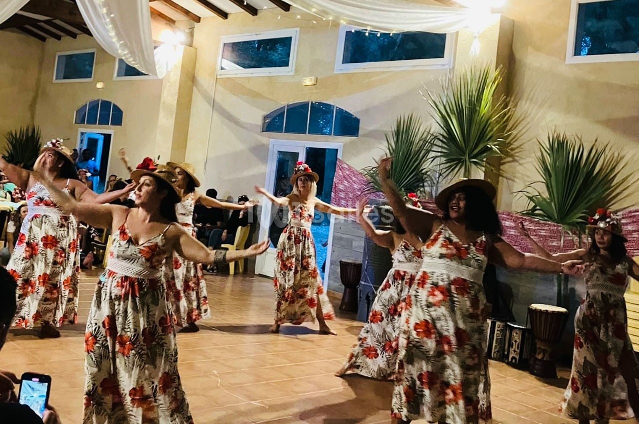 Des femmes en robes fleuries dansent en groupe dans une salle décorée, sous des lumières tamisées.