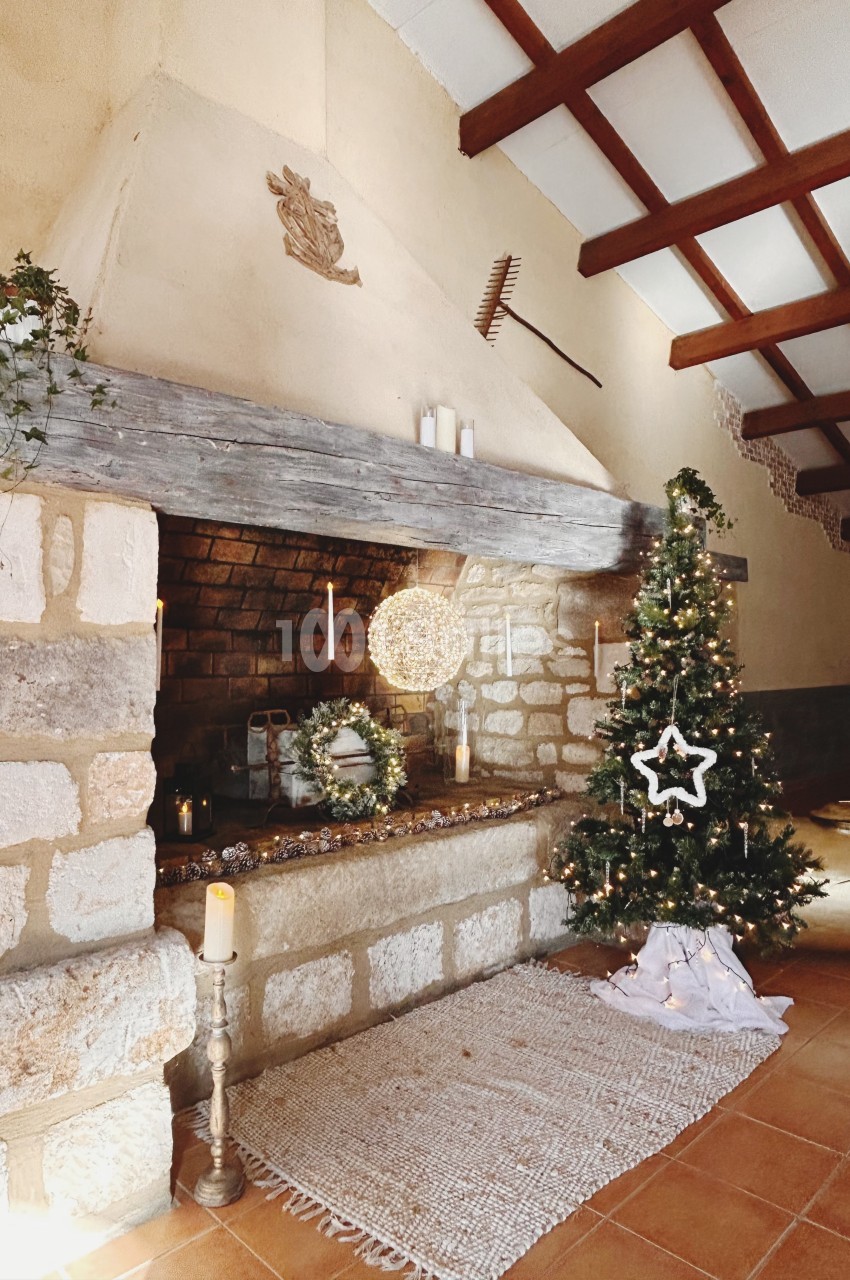 Cheminée en pierre décorée pour Noël avec un sapin illuminé, des bougies et une guirlande lumineuse.