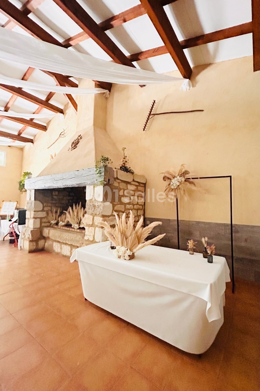 Cheminée en pierre dans une salle rustique avec une table décorée de fleurs séchées et un cadre métallique.