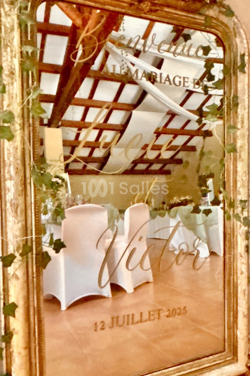 Miroir doré décoré de feuillage, reflétant une salle de réception avec des chaises blanches et un plafond en poutres…