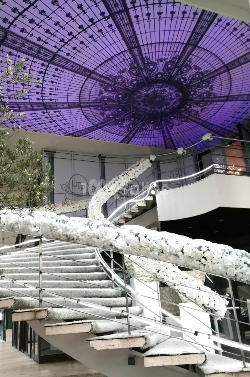 Escalier décoré de fleurs blanches sous une verrière violette ornée de motifs géométriques.