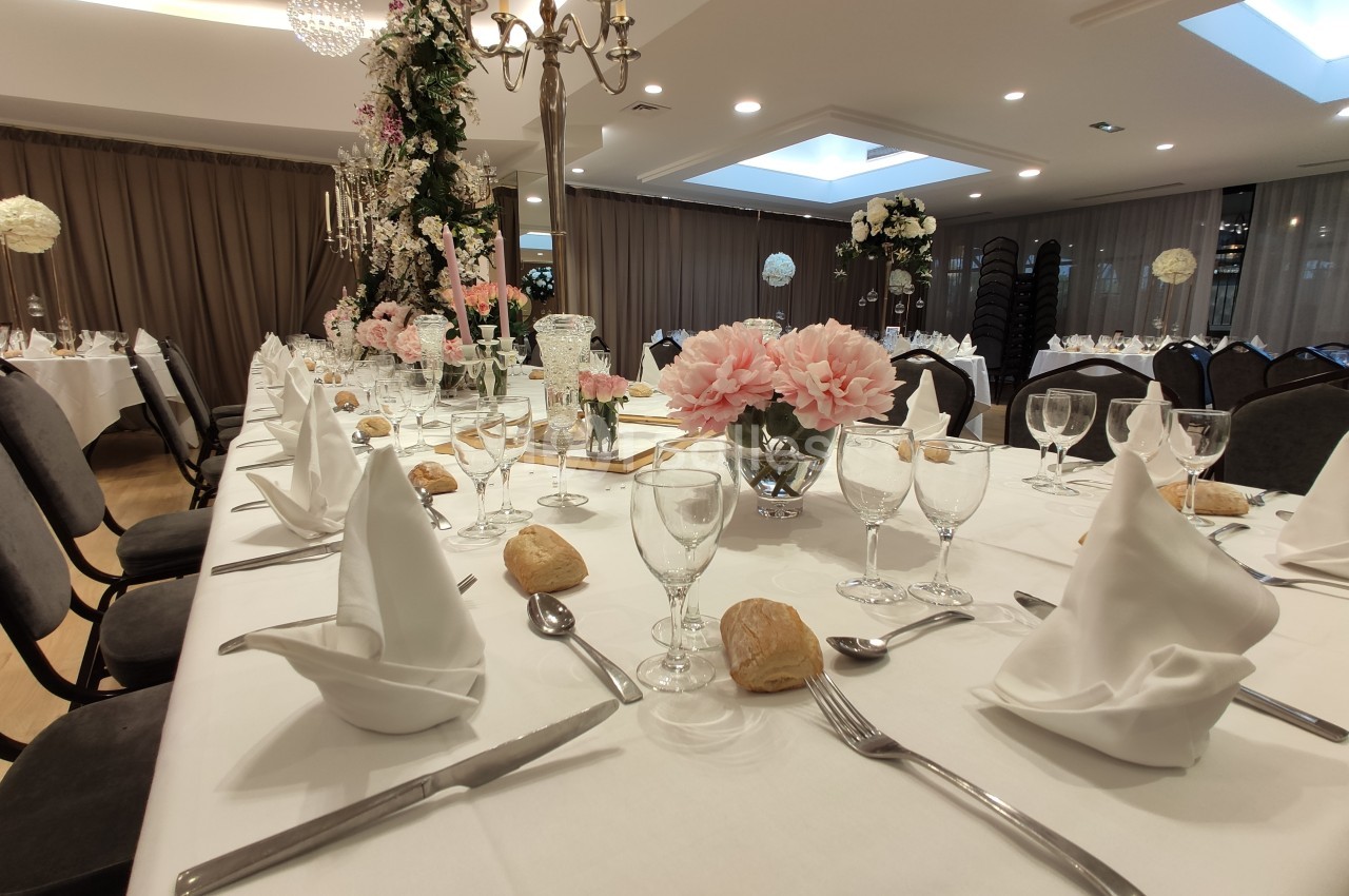 Table élégamment dressée pour un événement, avec serviettes pliées, verres, couverts et décorations florales.
